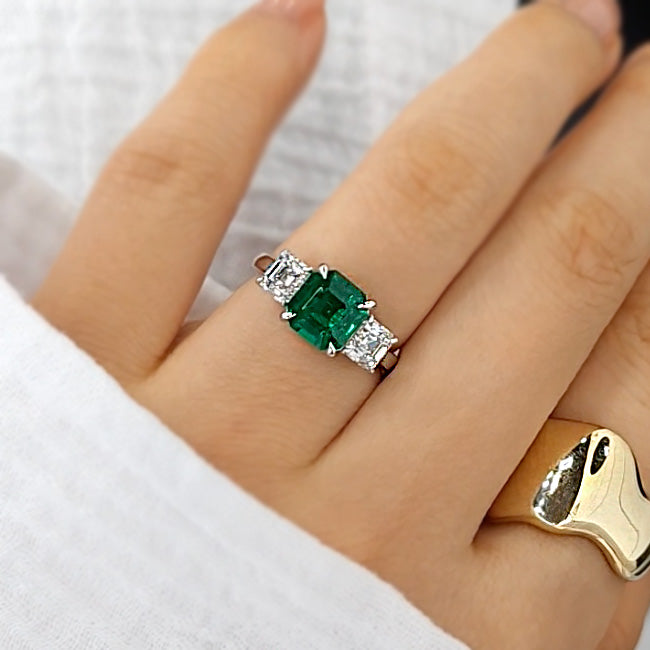 Green Emerald 3 Stone Engagement Ring with Asscher Diamond Side Stones and chunky gold ring on left hand