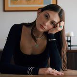 Woman wearing gold and emerald jewelry including rings, bracelets, and necklace.