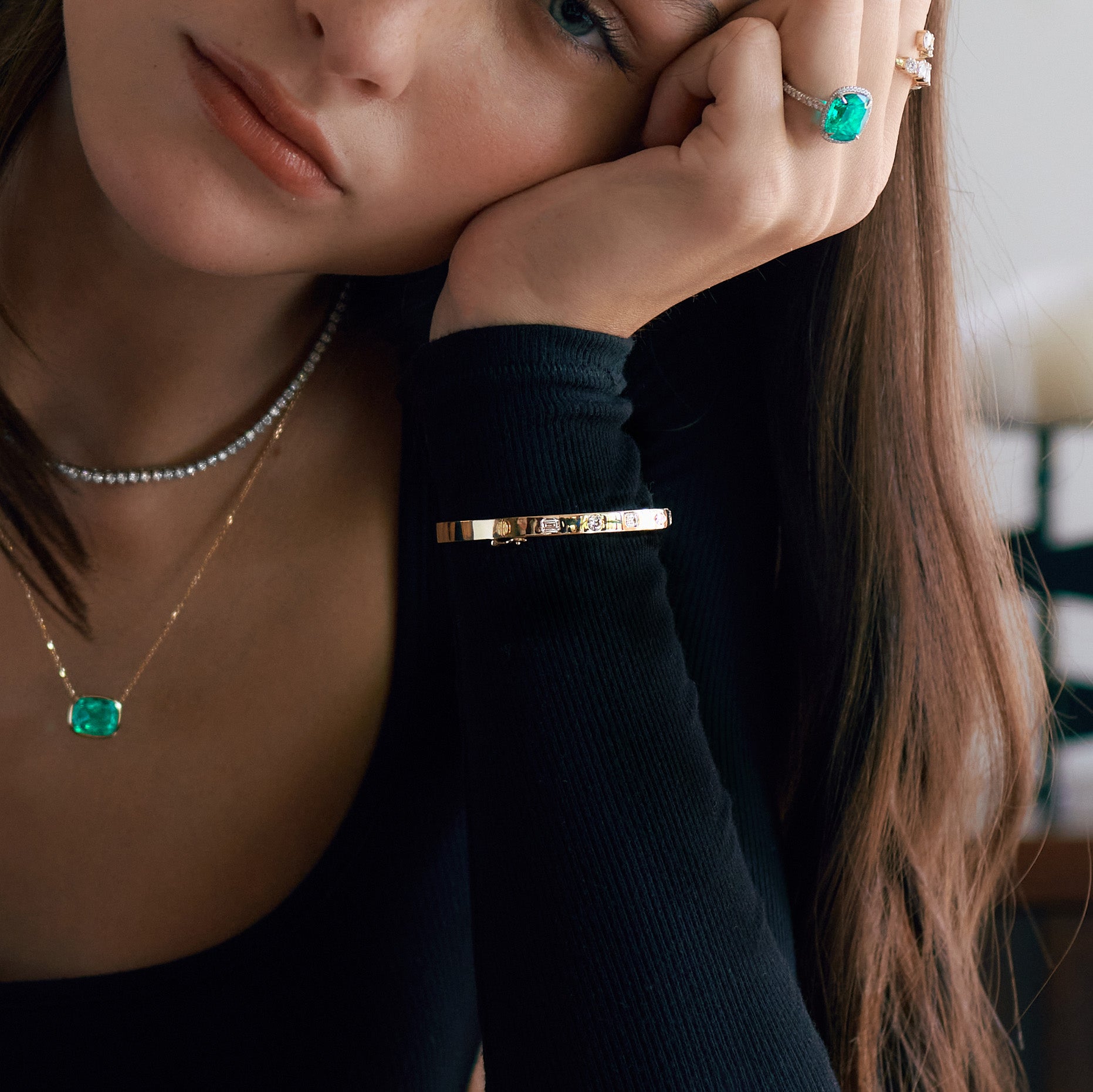 Closeup of gold bangle on a woman wearing gold and emerald jewelry.