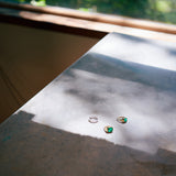 Two green emerald gold rings and a diamond ring on concrete surface.