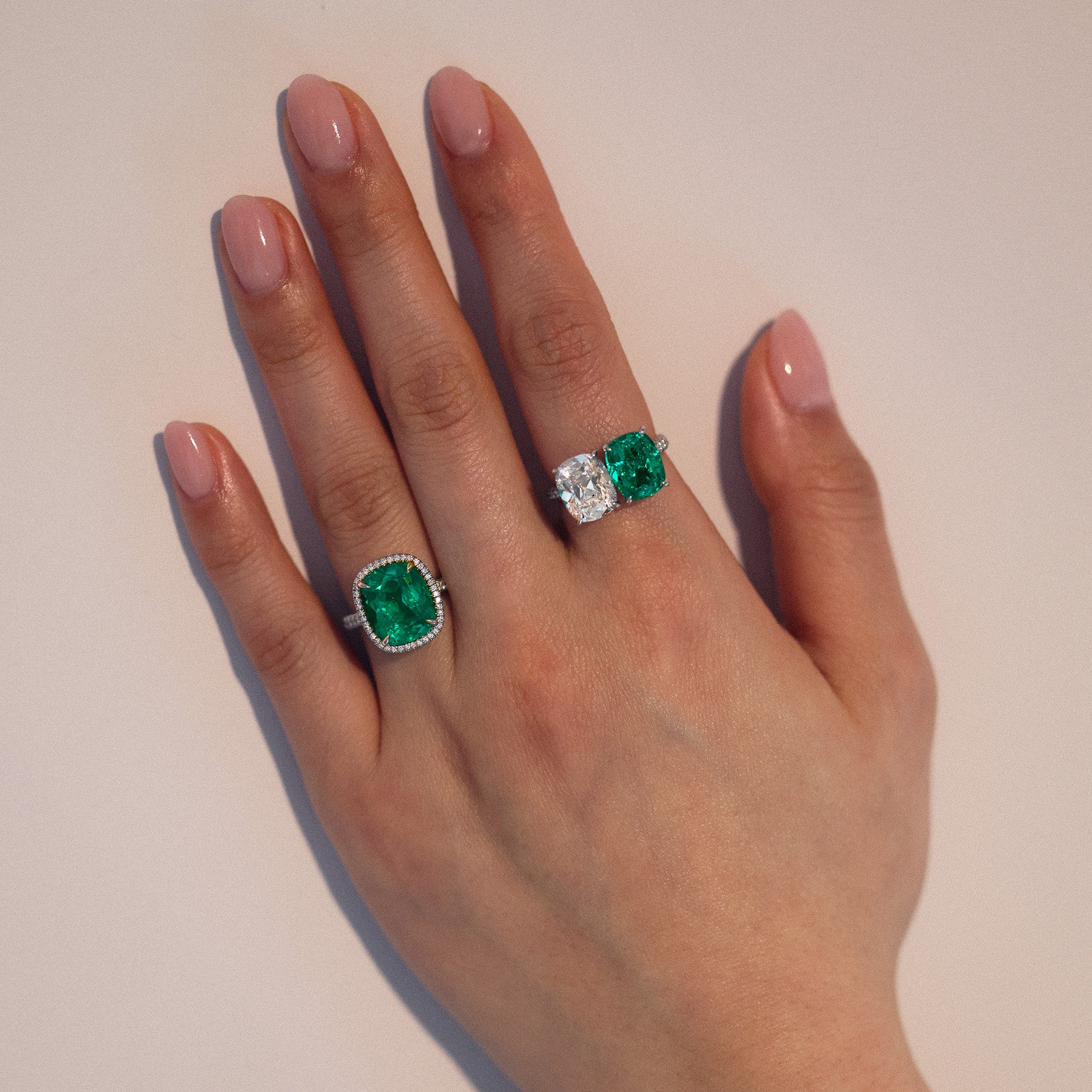 Closeup of woman's hand wearing green emerald and diamond rings.