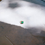 Green emerald gold ring on concrete surface.