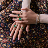 Two hands wearing green emerald gold rings and diamond jewelry.